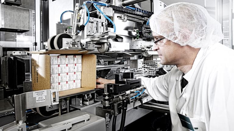 Man in white coat watching machine packing medicines